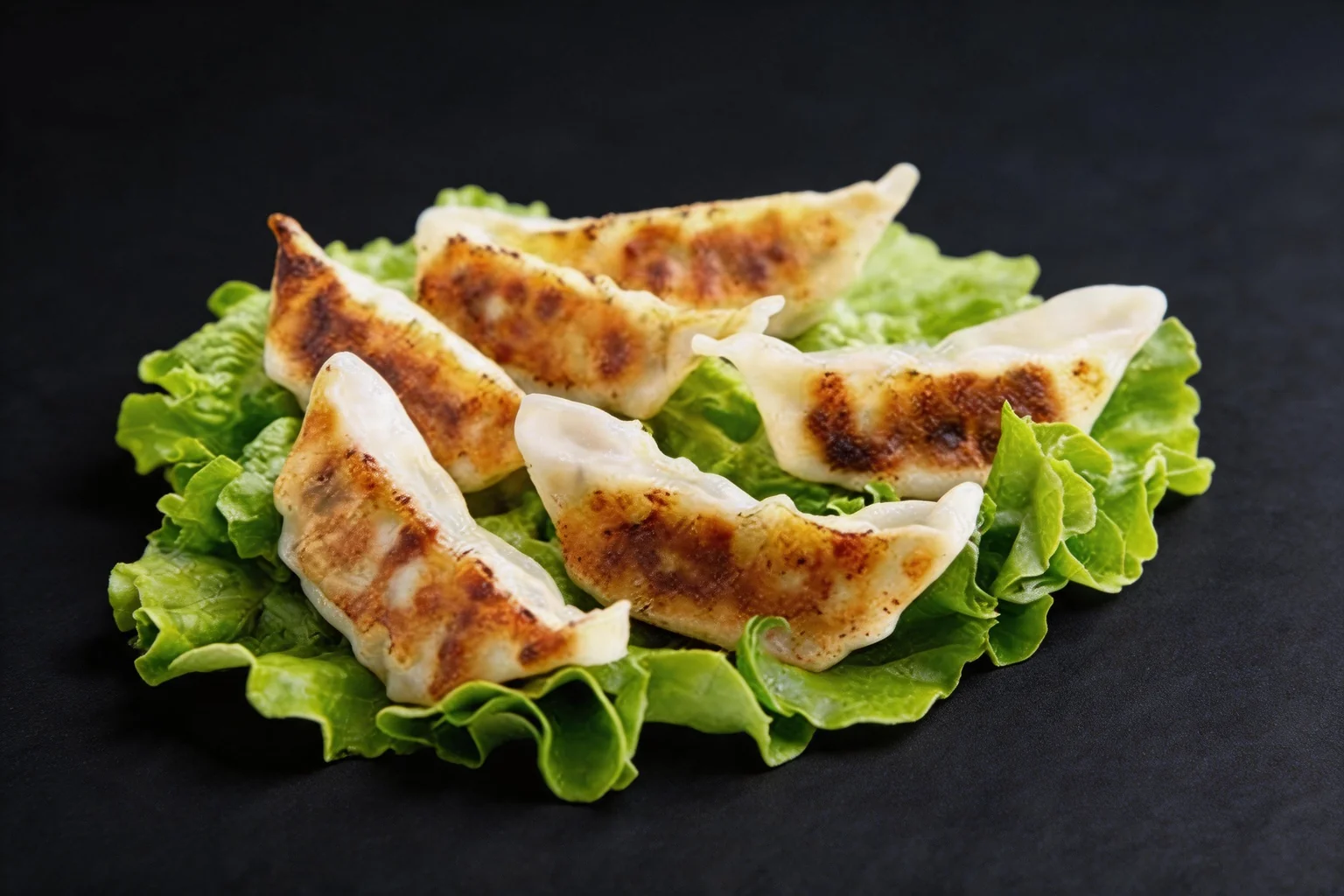 Golden pan-fried gyoza on a lettuce leaf, dark background.