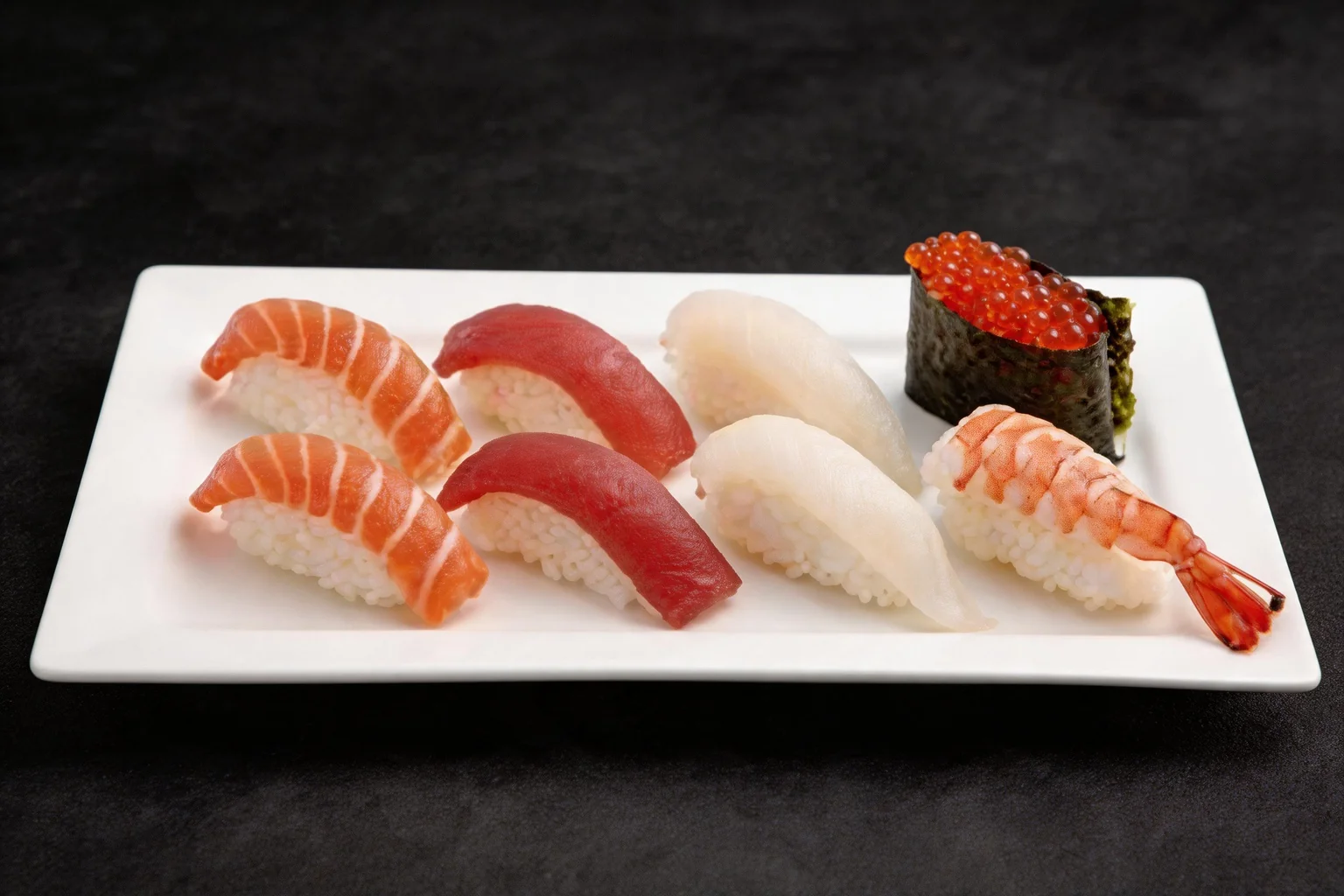 White plate with an assortment of sushi: salmon, tuna, white fish, shrimp and a salmon roe gunkan.