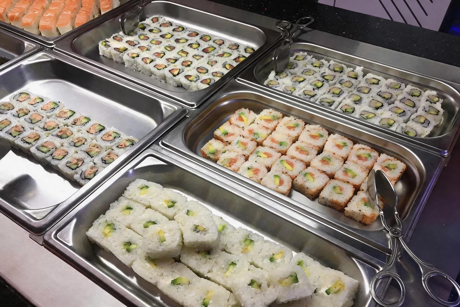 Stainless trays of salmon and avocado maki and California rolls.